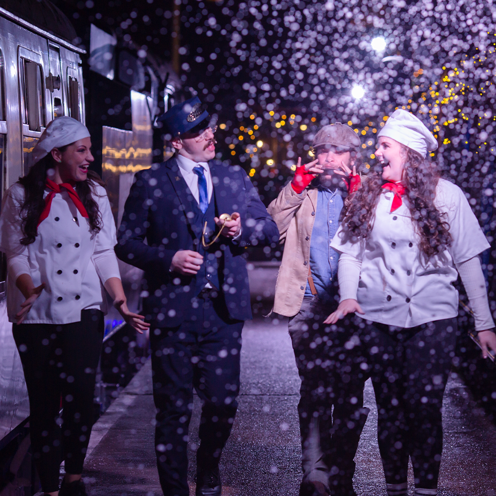 Chef, conductor, hobo and another chef walking outside on the platform in character underneath snow flurry 